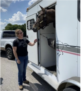 Christian standing next to a horse trailer containing her horse, Junior.